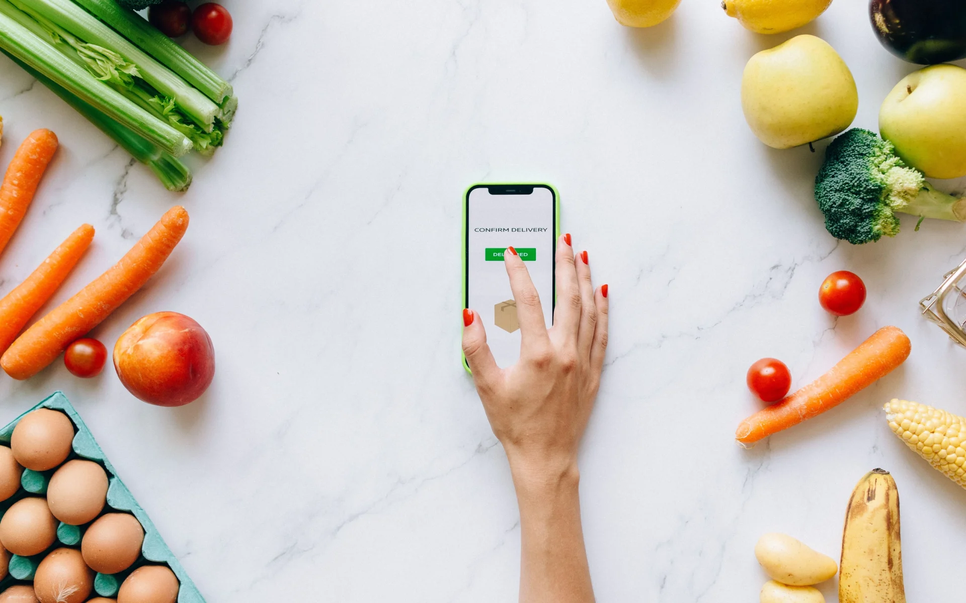 Mano confirmando un pedido en el teléfono entre frutas y verduras: caso conceptual de app para mercado fresco