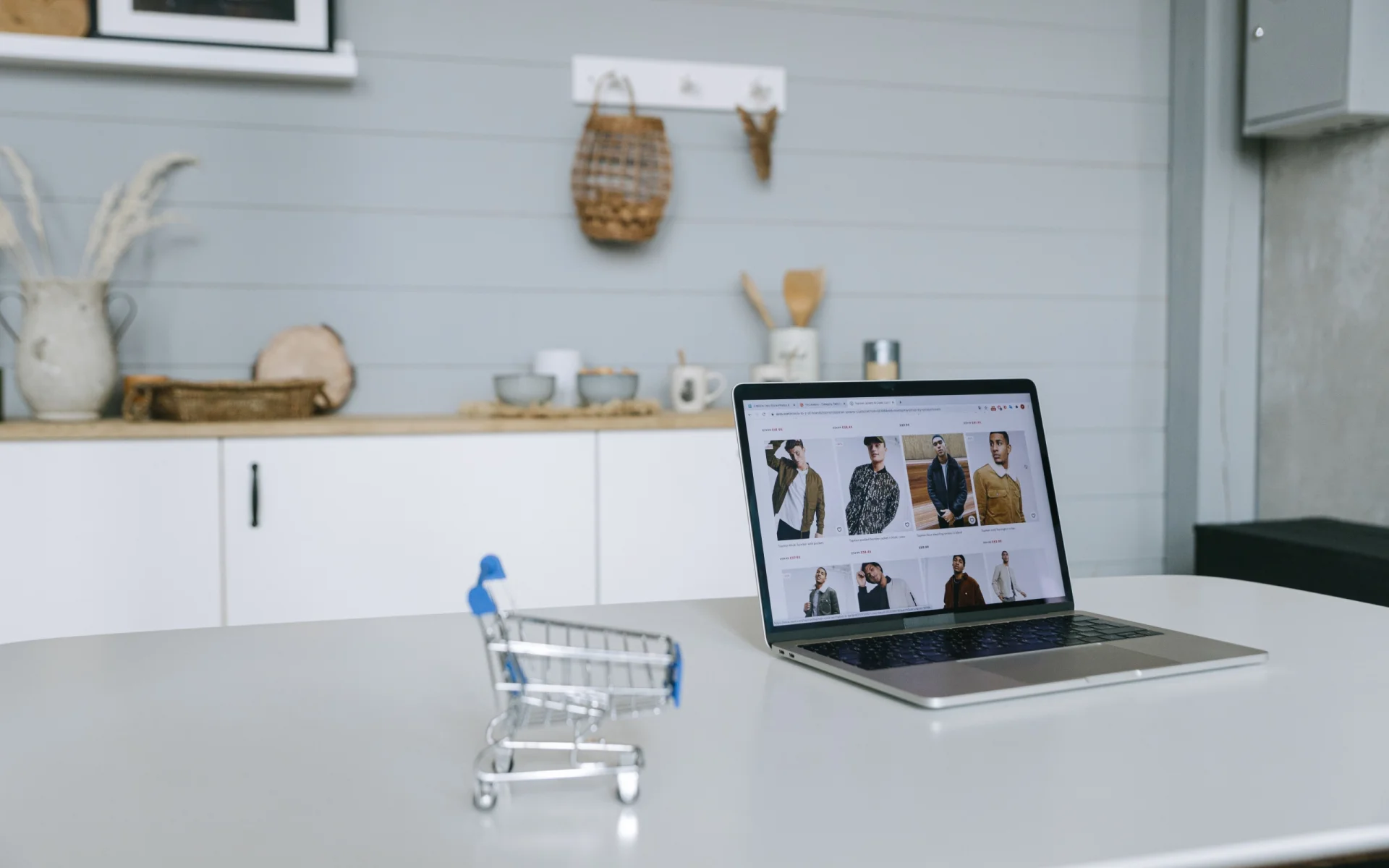 Laptop con catálogo de ropa junto a un carrito miniatura: caso conceptual de tienda de moda en línea