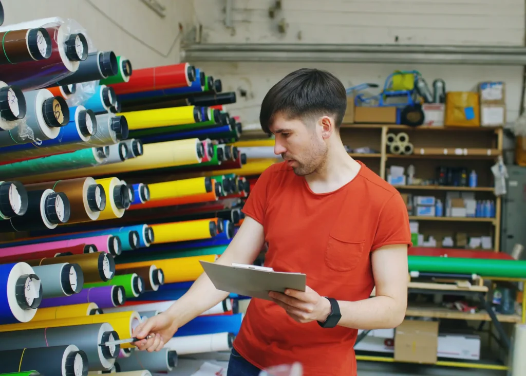 Operario del taller eligiendo rollos de vinil de colores para producir piezas con la marca del cliente