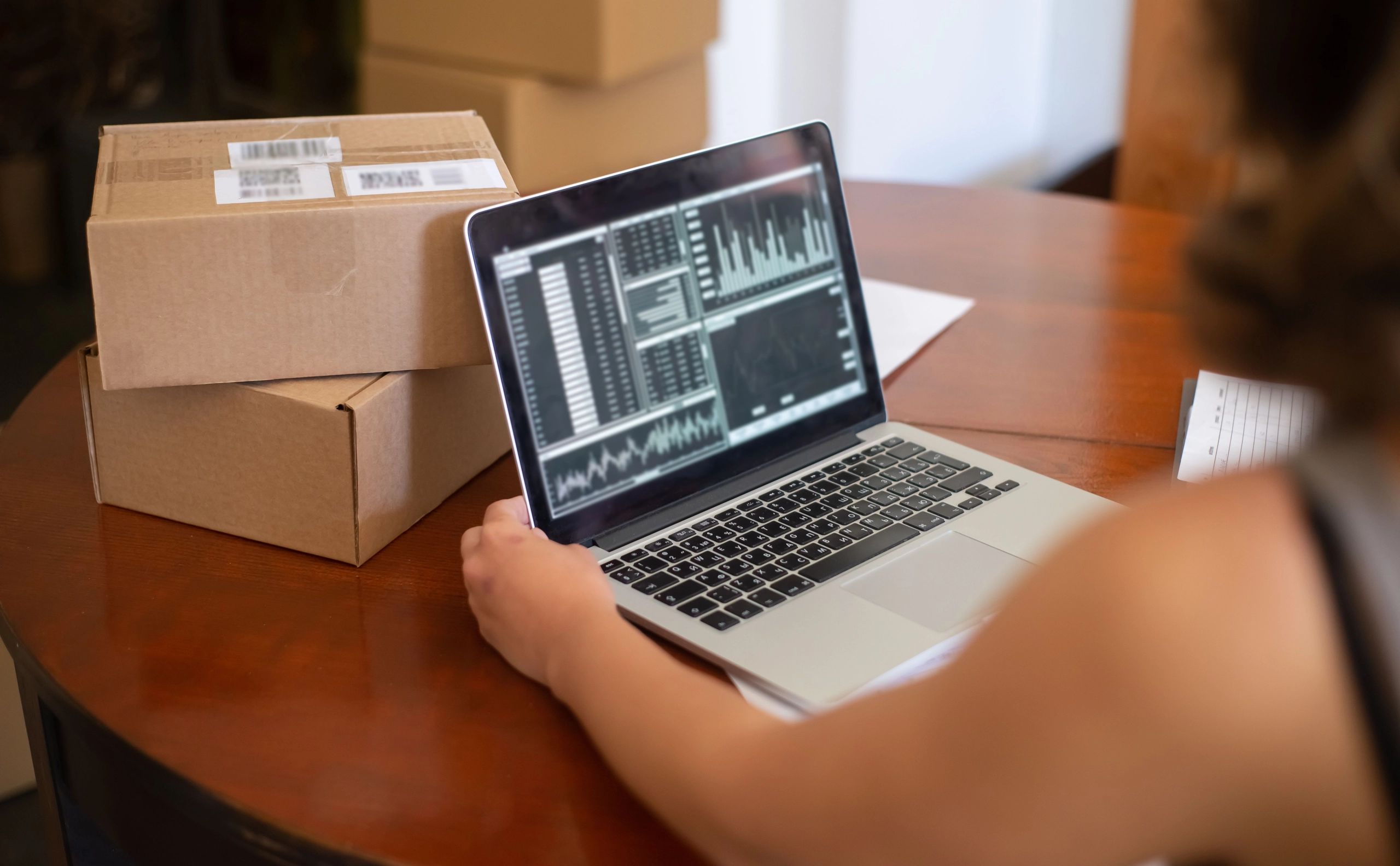Tienda en línea: laptop con panel de ventas e inventario junto a cajas de pedidos listas para enviar.